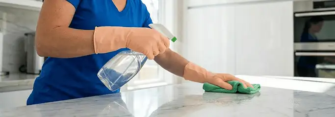 Maid service worker spraying and wiping a kitchen countertop with a microfiber cloth for sanitizing, Scottsdale, AZ.