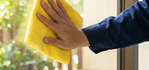 House cleaner wiping a glass window with a yellow microfiber cloth for streak-free cleaning, Scottsdale, AZ.
